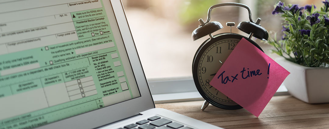 Laptop displaying tax forms and clock with "Tax time" note