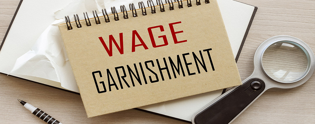 Wage Garnishment notebook, magnifying glass, and pen for IRS rules in North and South Carolinas.