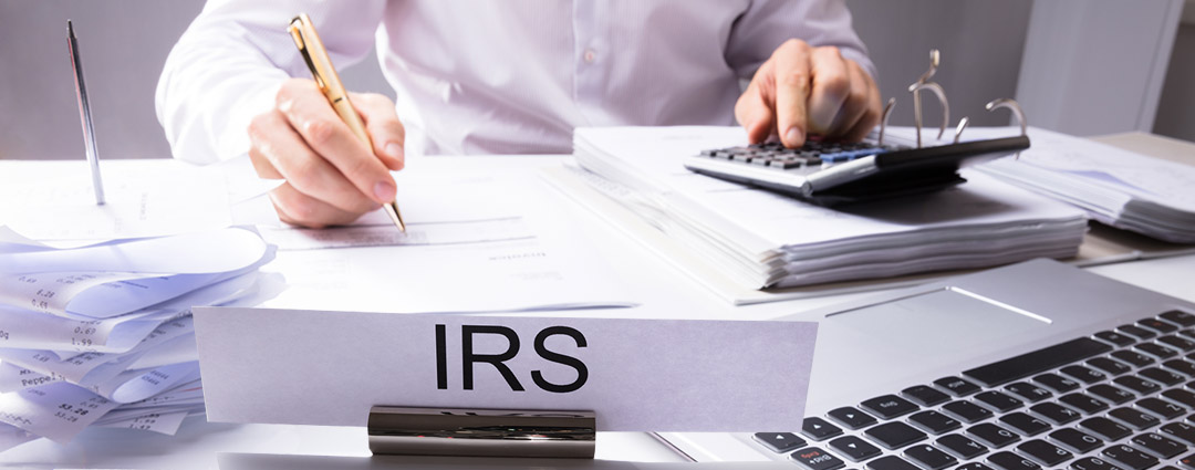 A desk sign for "IRS" with an agent reviewing documents, related to a Revenue Officer Visit in The Carolinas