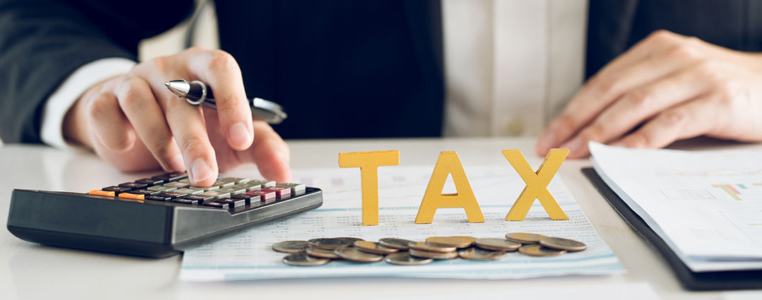 Professional using a calculator with "TAX" letters and coins for financial tax planning.